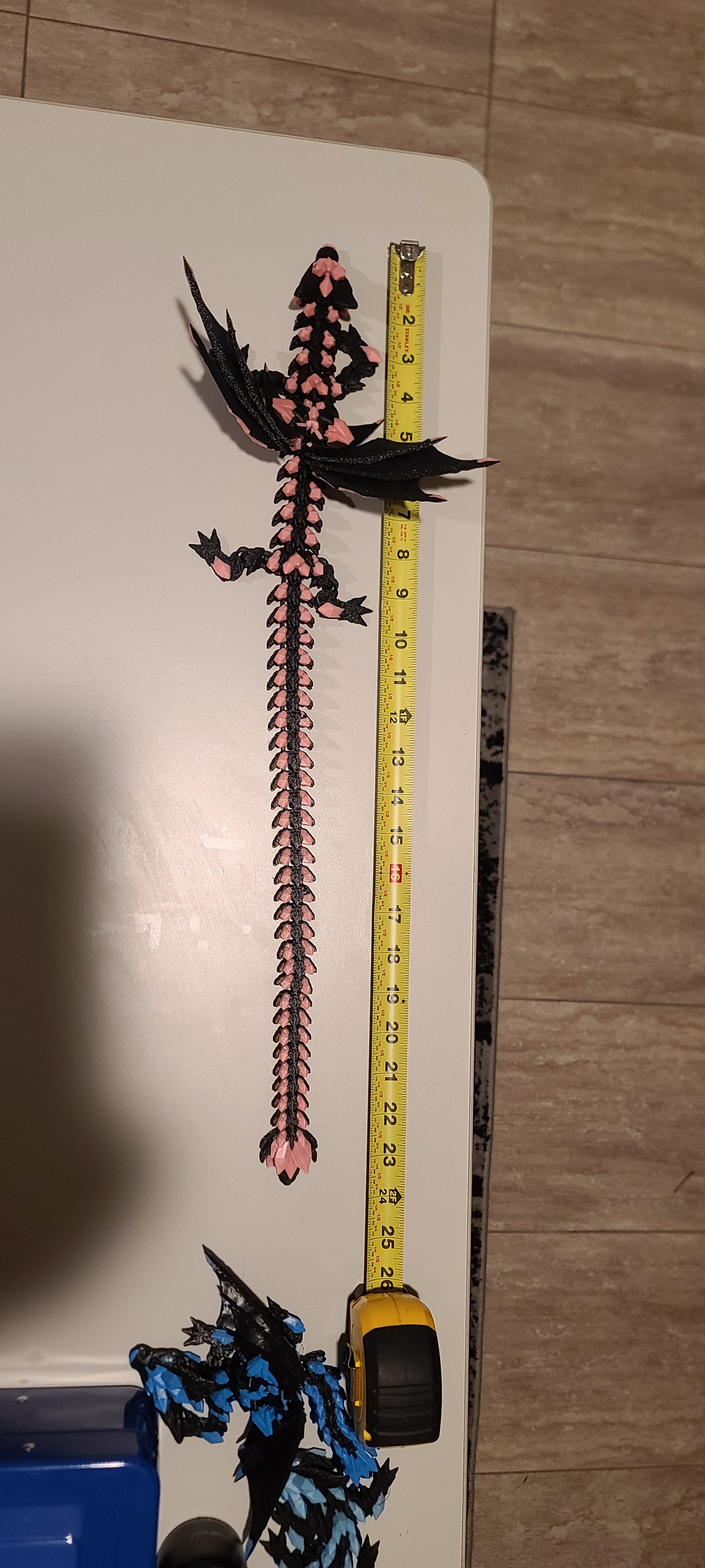 Peach and black colored dragon measured with measuring tape on a white background near a wood pattern floor. There is a blue and black dragon at the bottom of the image also.