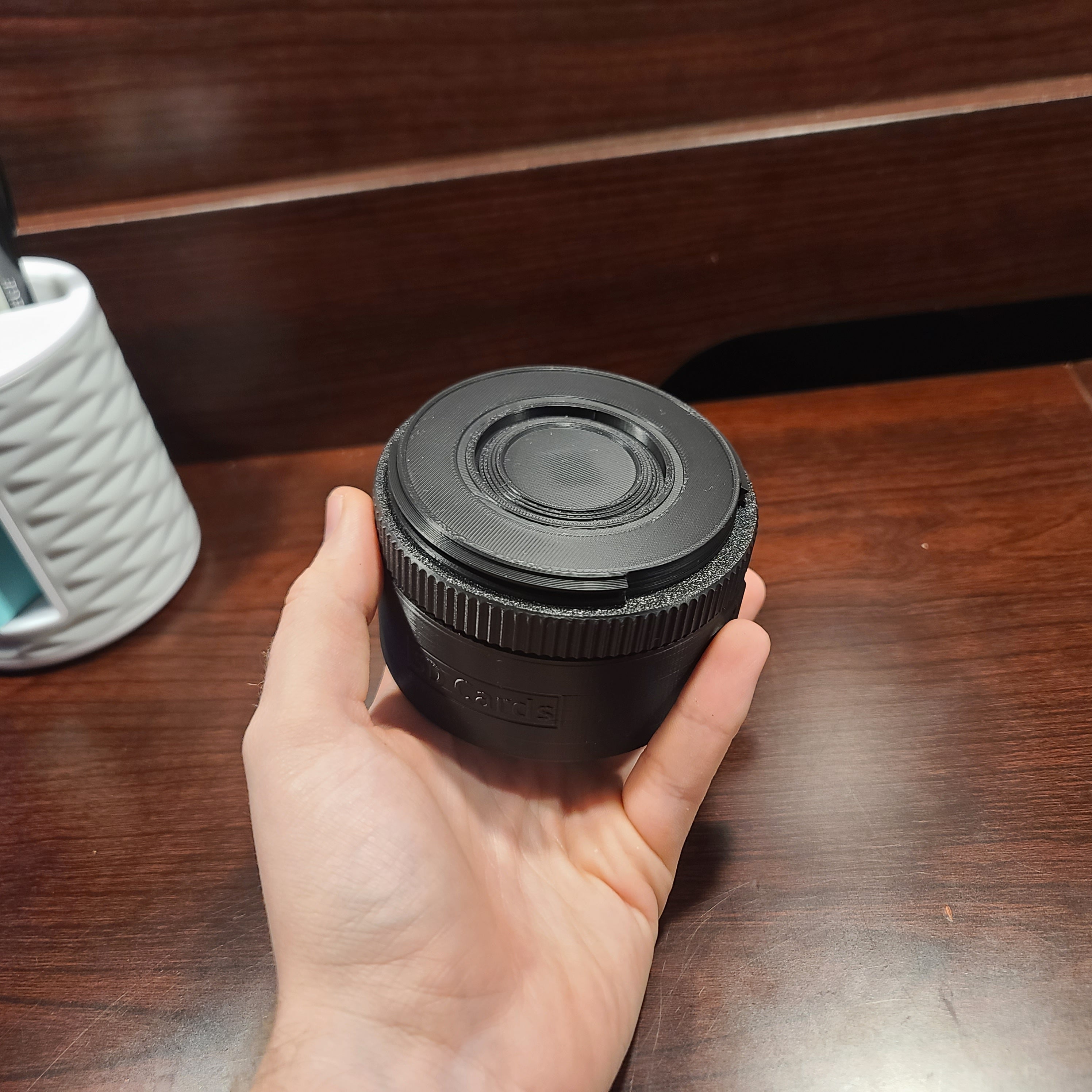 hand holding an sd card holder that spins to display the sd cards. Thumb finger is spinning the focal dial to select the sd card. There is a wood table in the background. The cover is applied so that no SD cards are visible or can fall out.