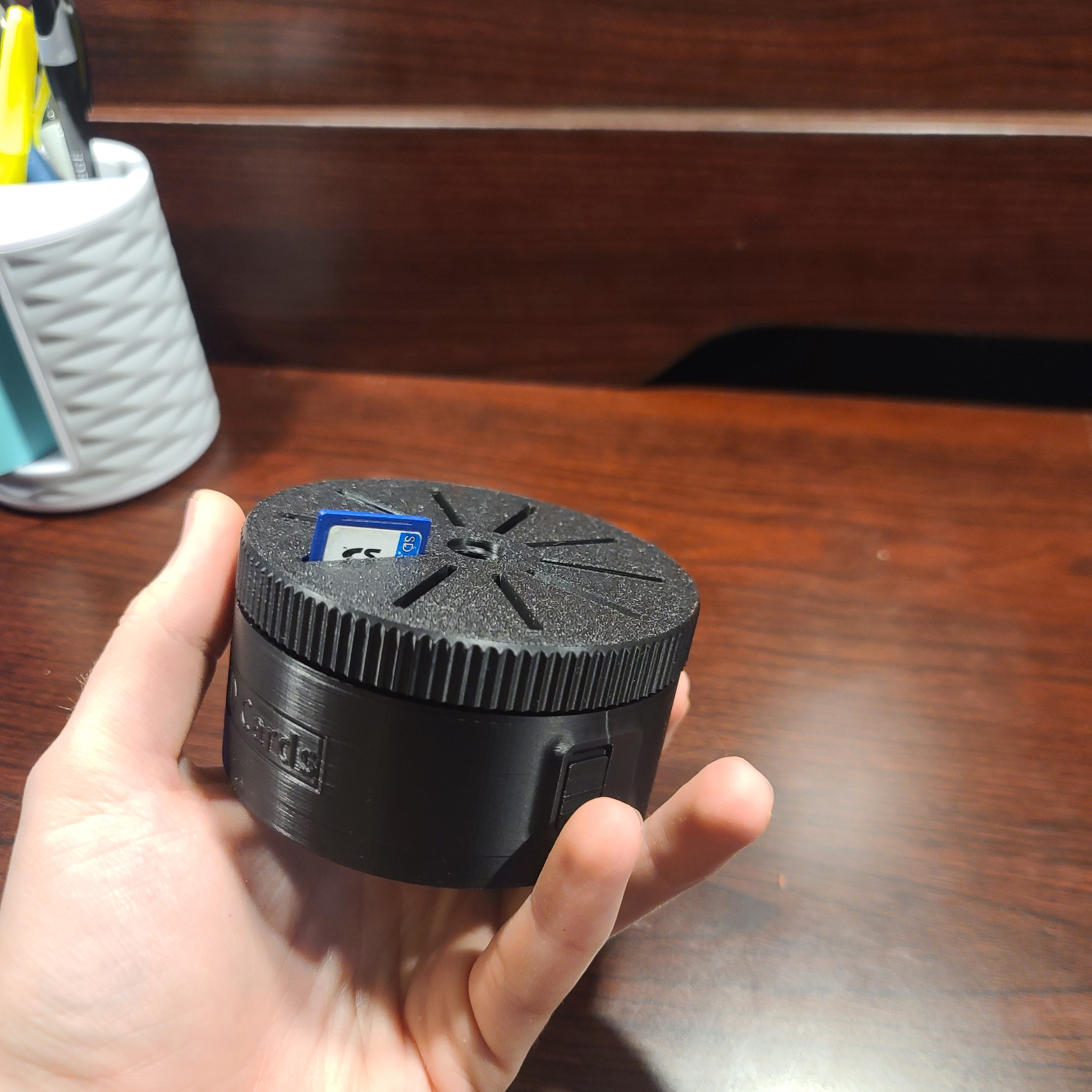 hand holding an sd card holder that spins to display the sd cards. Thumb finger is spinning the focal dial to select the sd card. There is a wood table in the background.