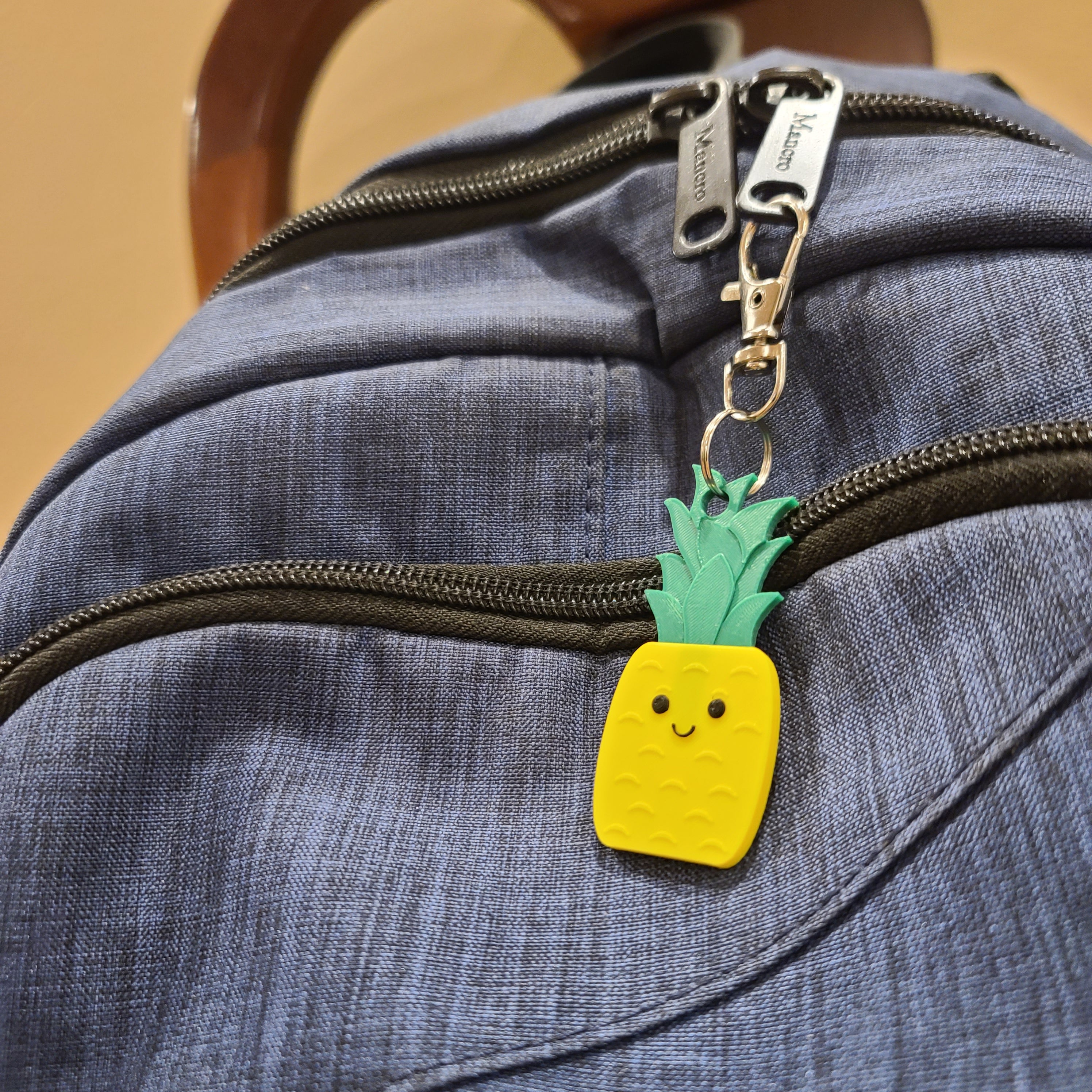 brown chair with a blue bag. blue bag has a pineapple keychain or key charm attached to one of the zippers.