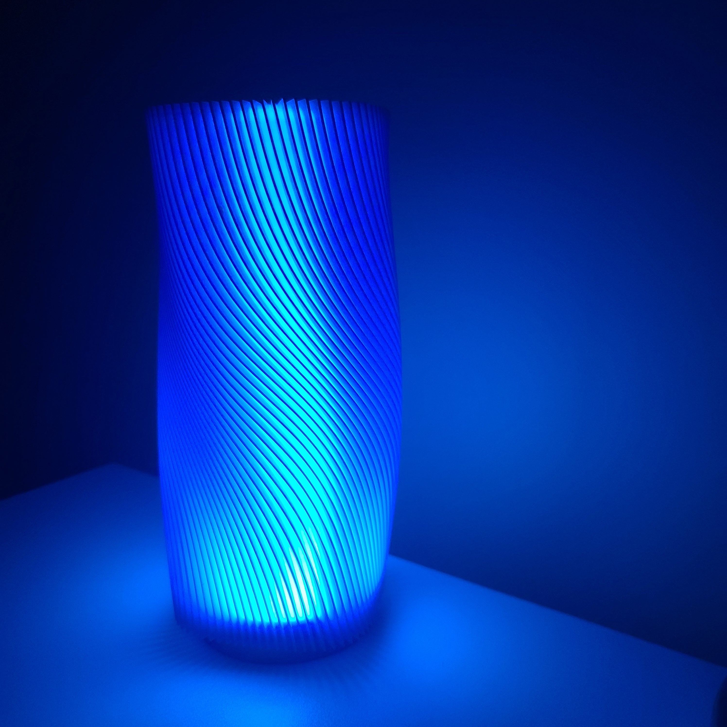lamp on a white nightstand emiting a blue light due to a blue lampshade with a wavy design