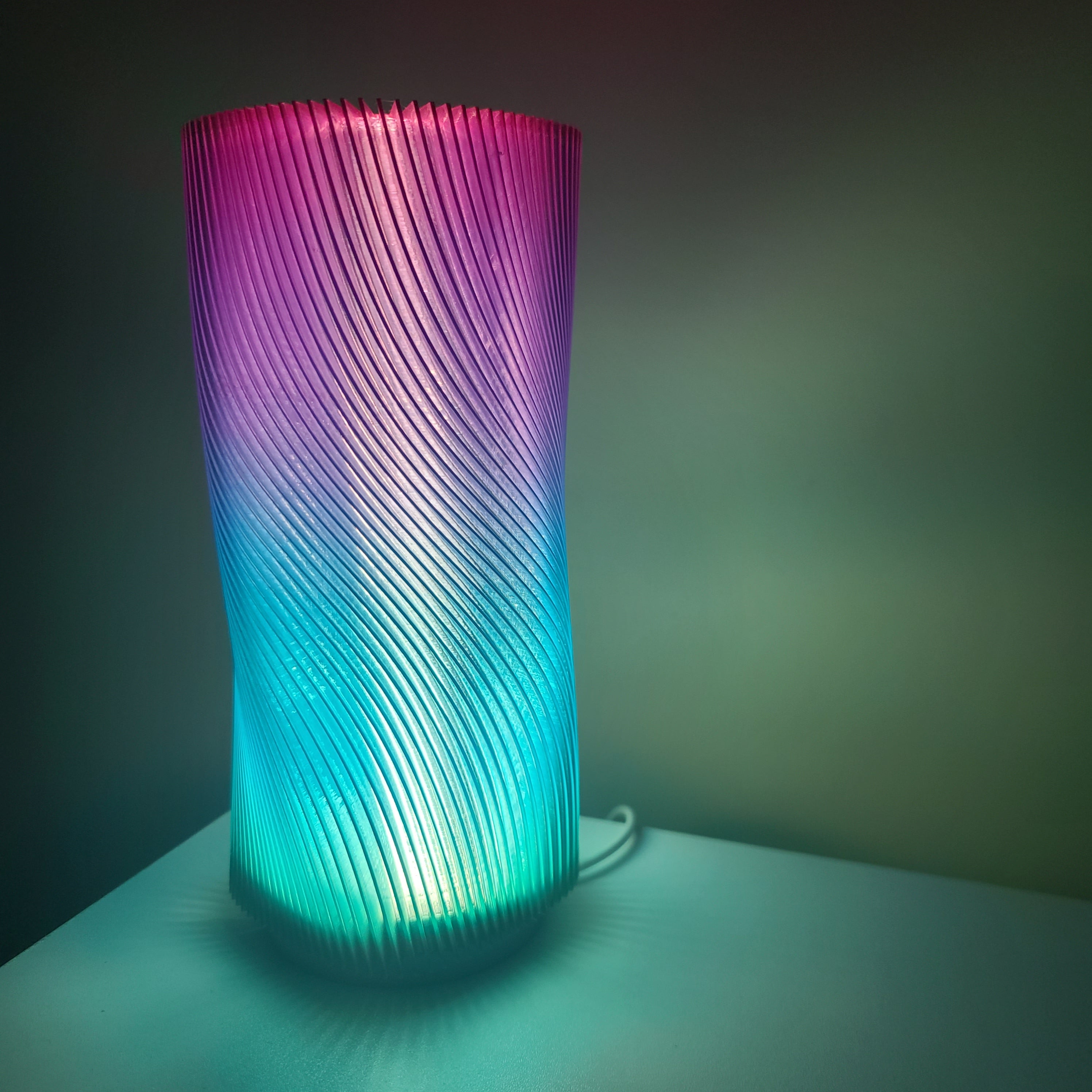 lamp on a white nightstand emitting a gradient of colors including green, blue, and purple.