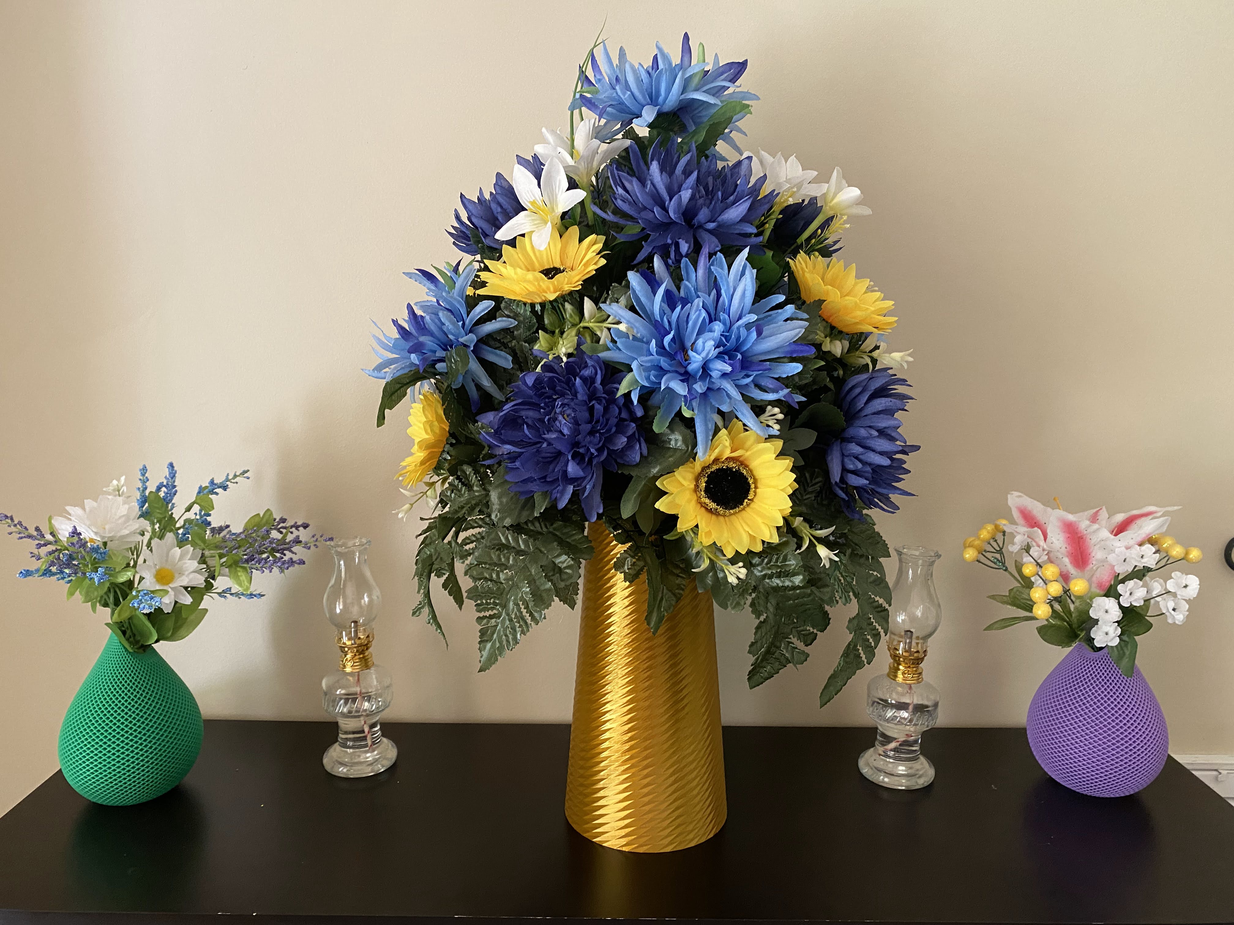 Vases displayed with flowers inside. The left is green, the center is gold, and the right vase is purple.