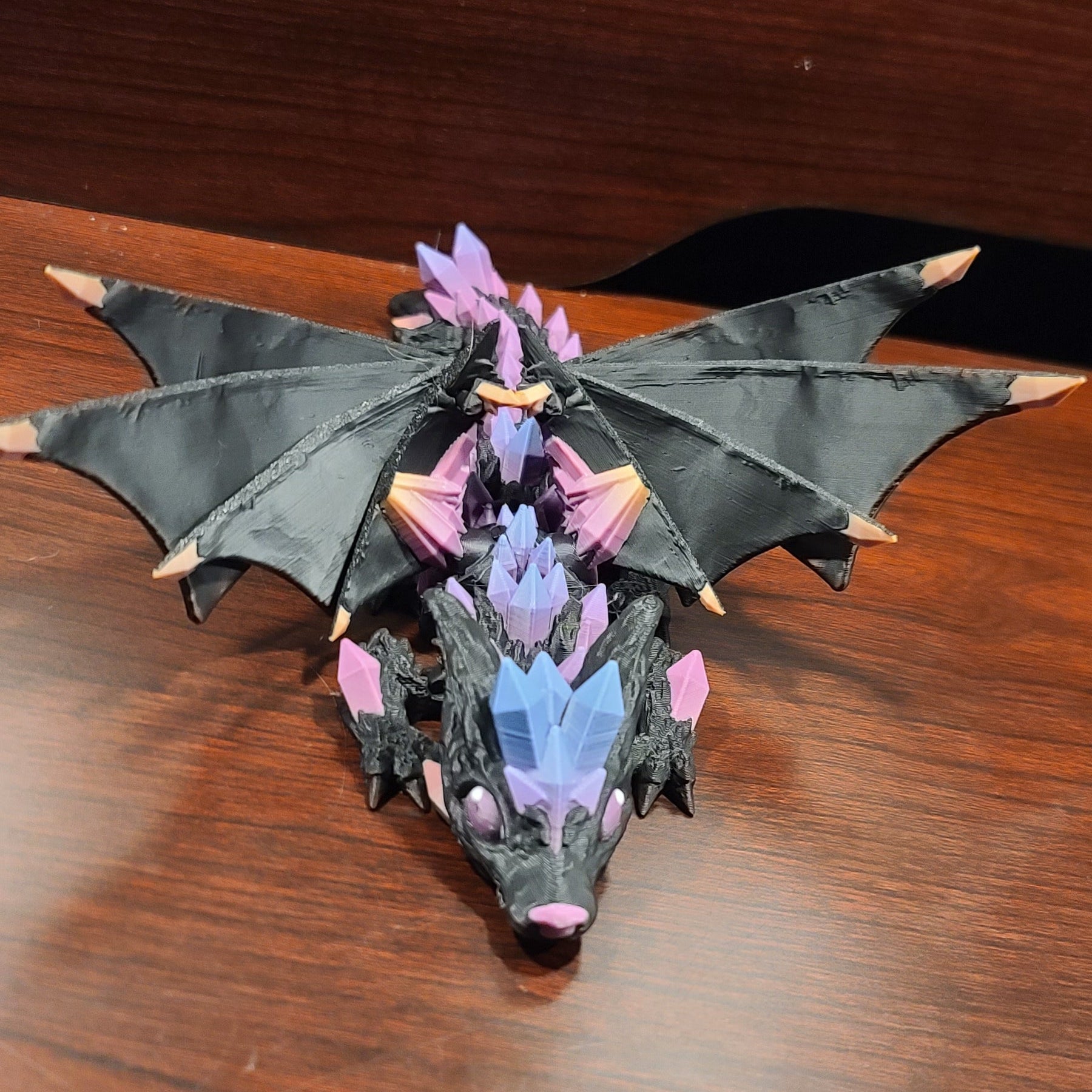 wood table with a wooden back and a crystal wolf dragon fidget with wings atop or on top of the table. The crystals are rainbow crystals.