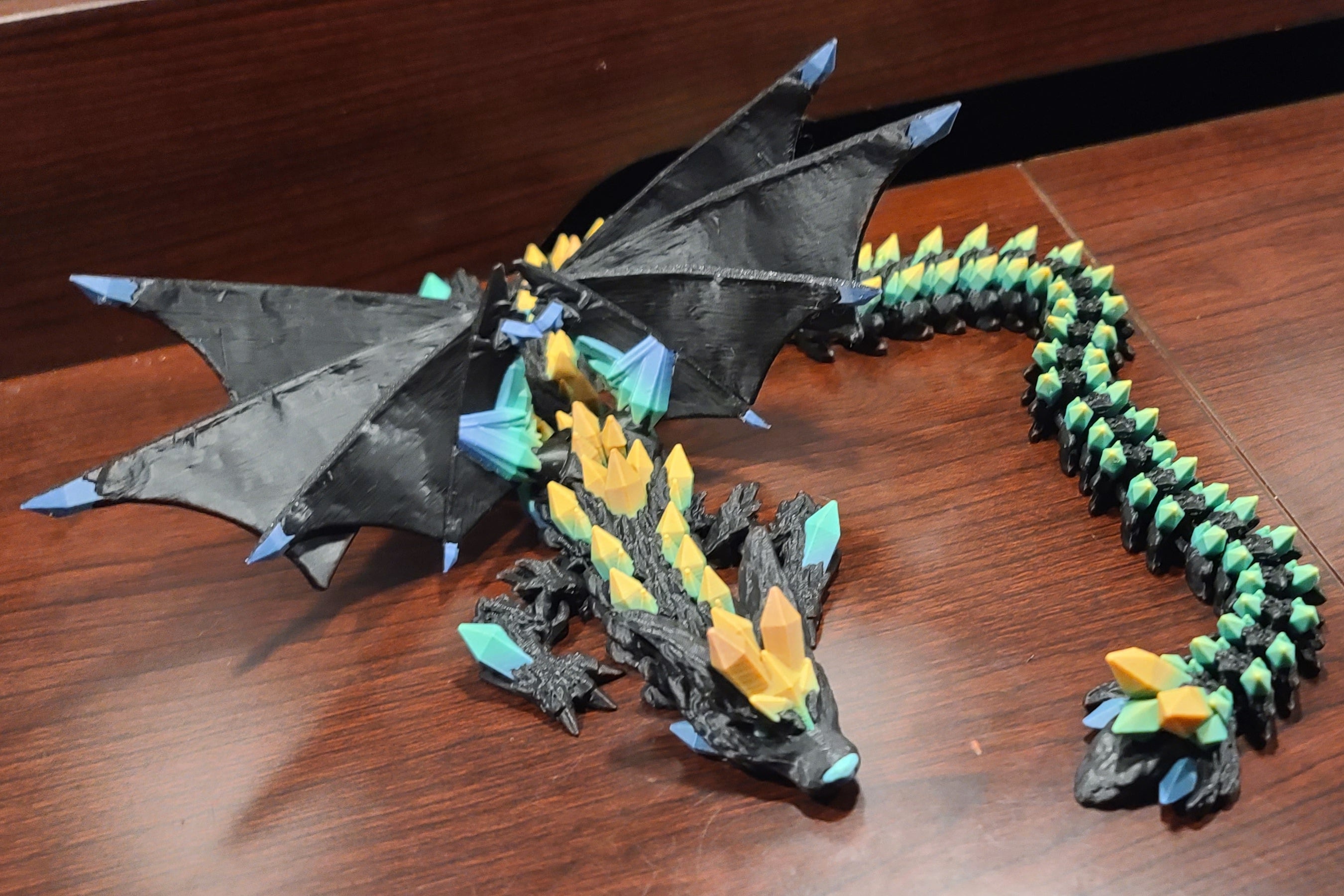 wood table with a wooden back and a crystal wolf dragon fidget with wings atop or on top of the table. The crystals are rainbow crystals.