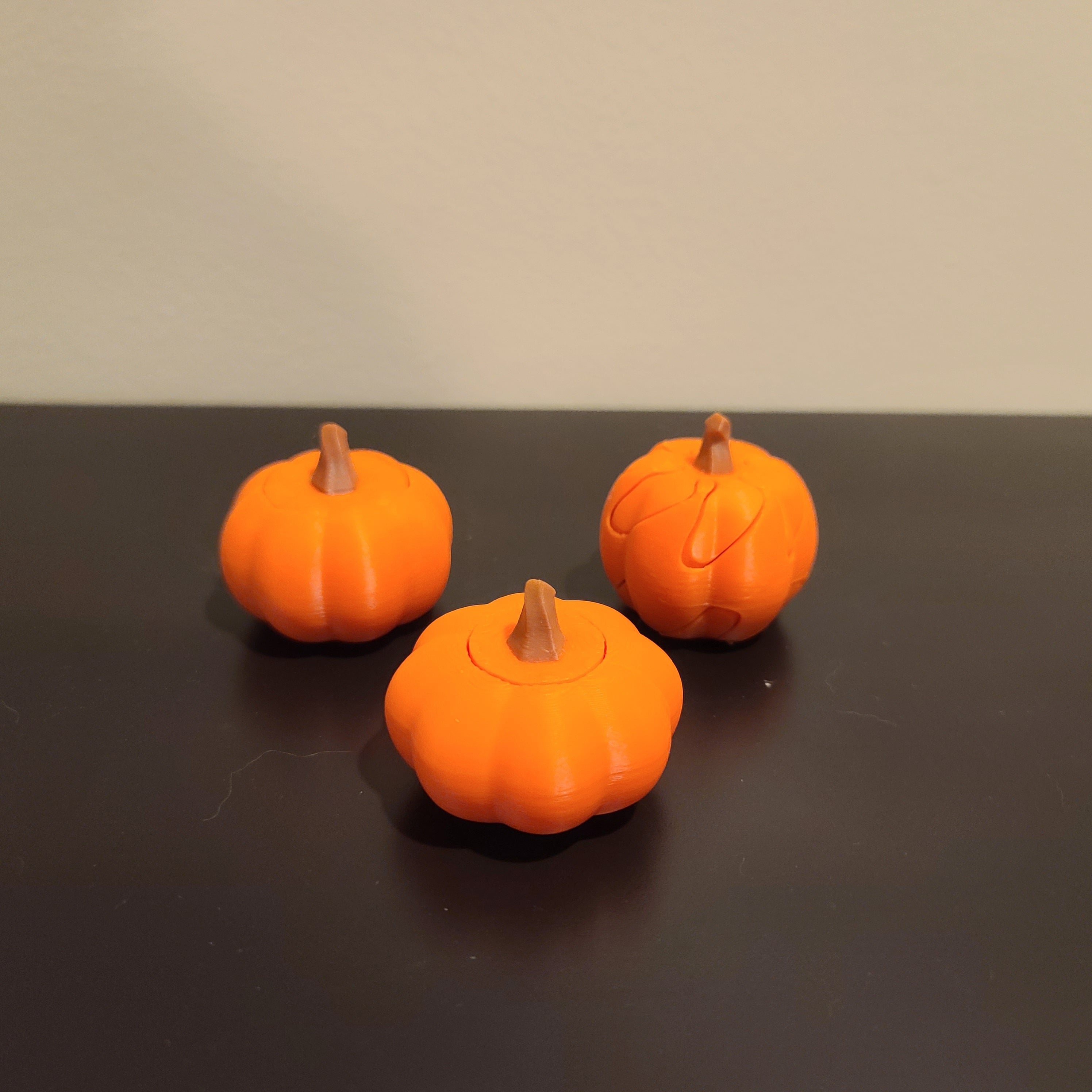 three pumpkin fall fidgets on a black table with a tan wall in the background.