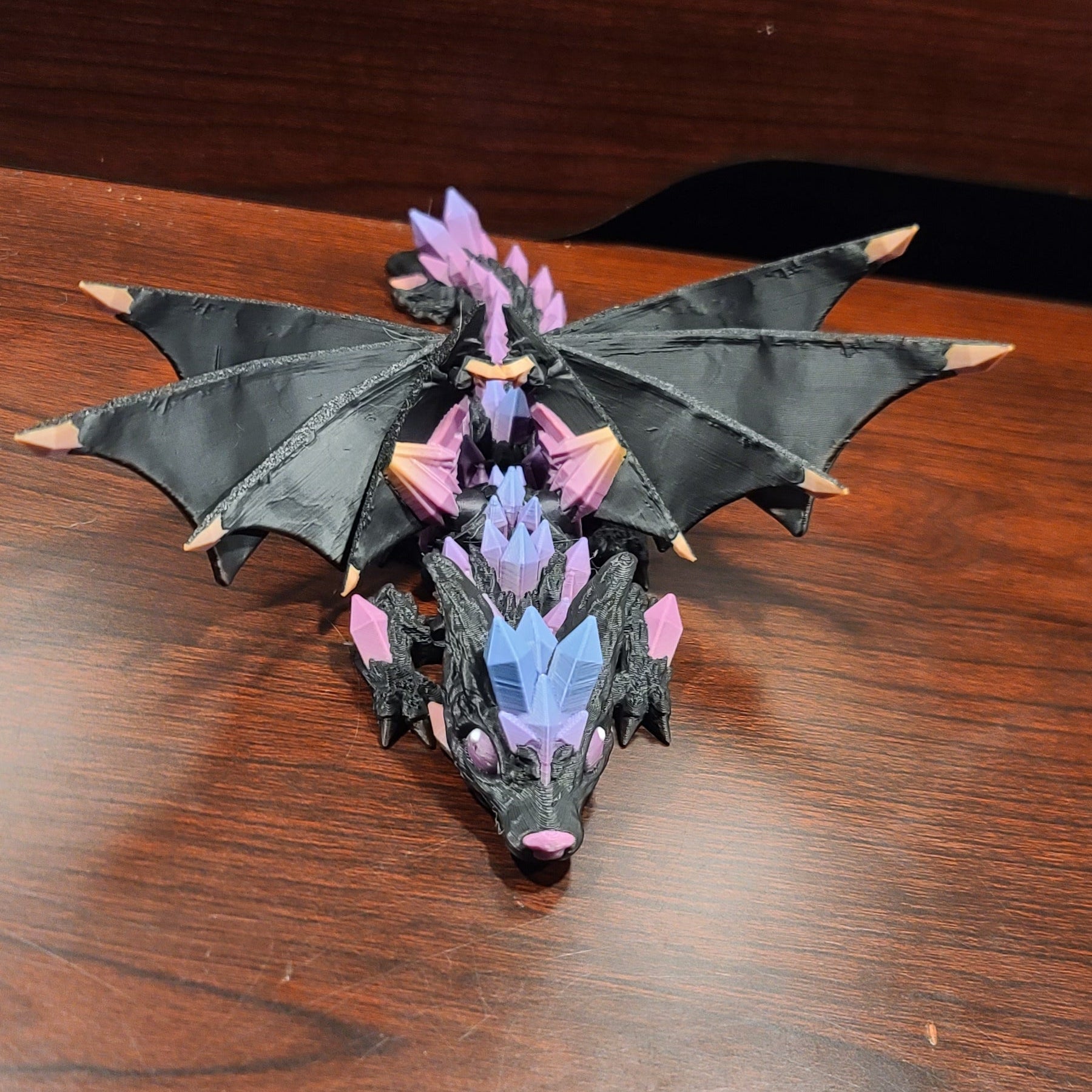wood table with a wooden back and a crystal wolf dragon fidget with wings atop or on top of the table. The crystals are rainbow crystals.