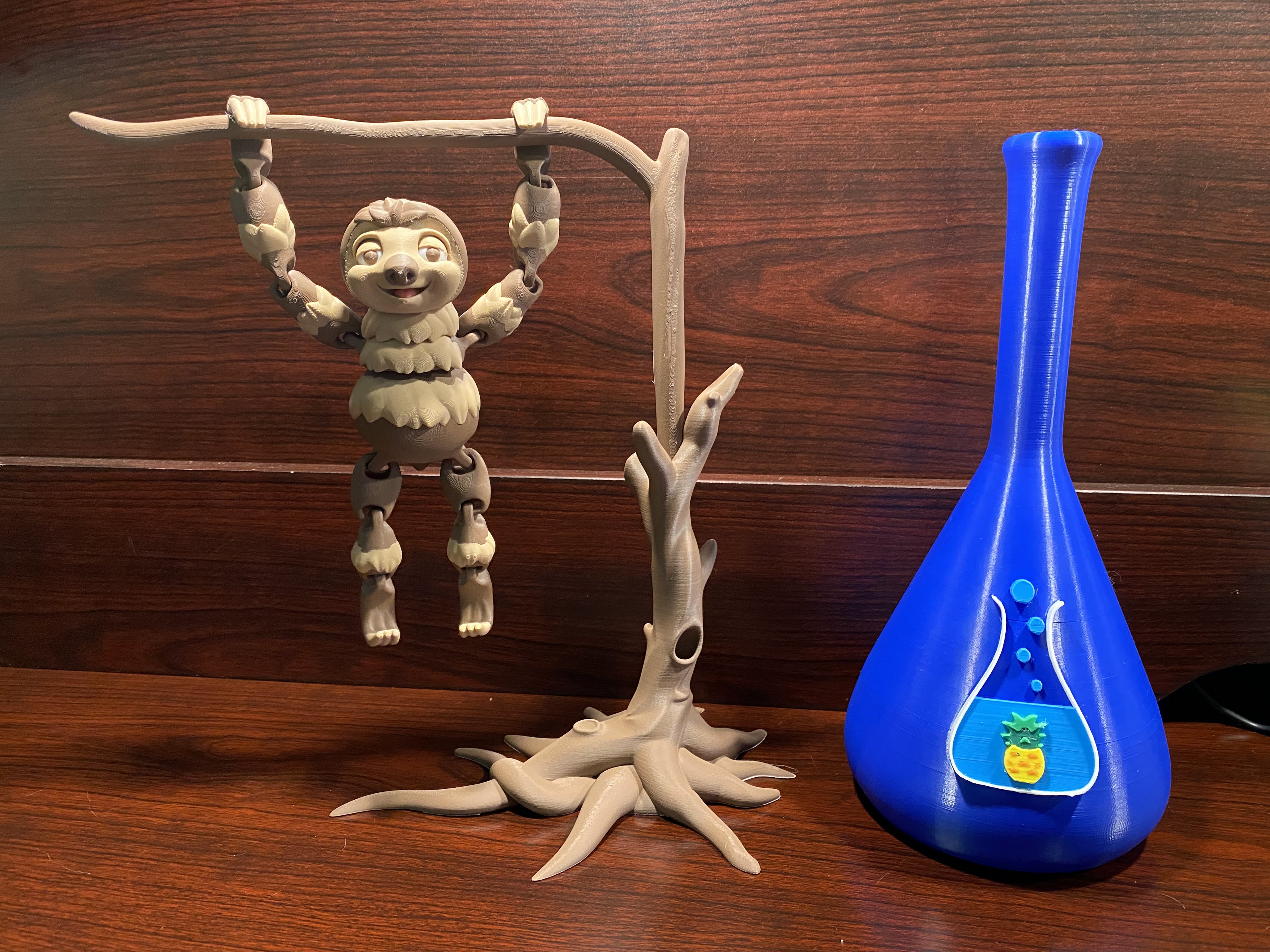 Sloth hanging on tree limb on wood surface next to blue beaker.