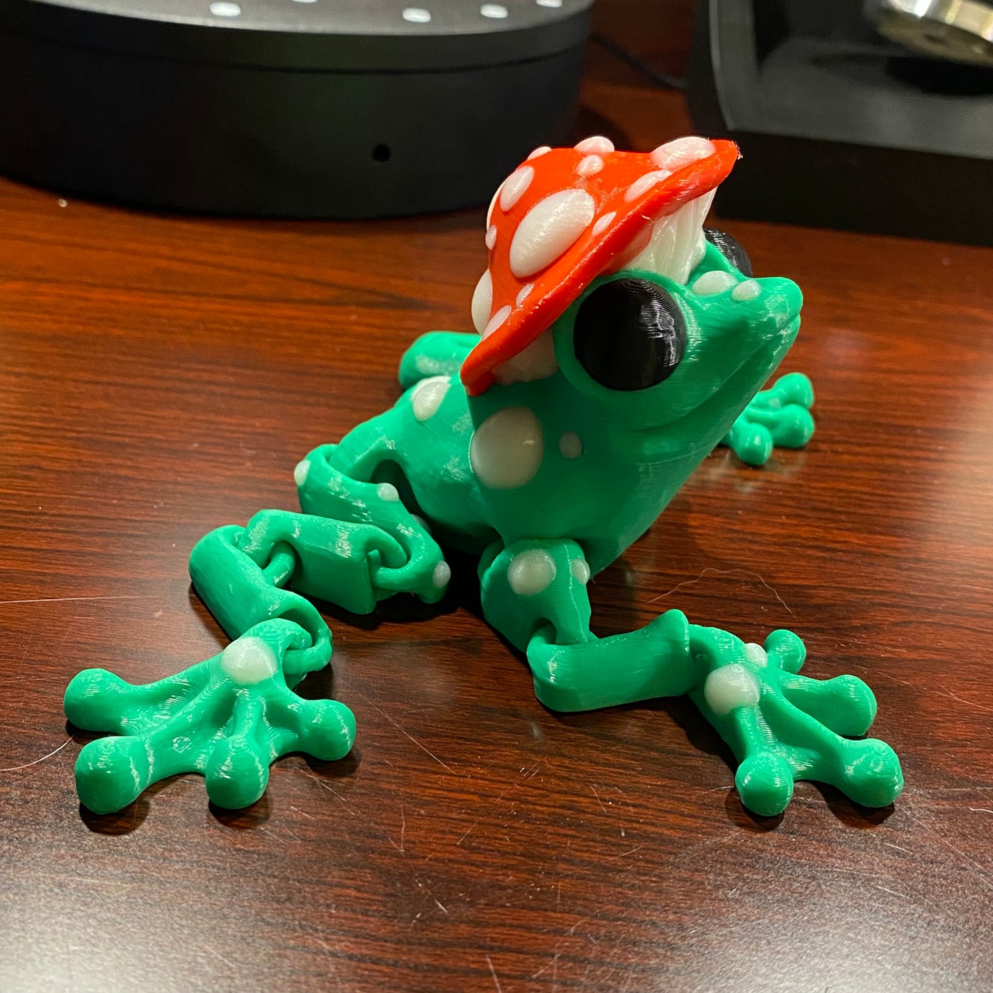 Green jumbo frog with a mushroom hat on a cherry wood desk