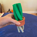 Hand holding a small terracotta pot with green markers on a blue surface.