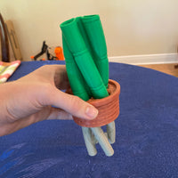 Hand holding a small terracotta pot with green markers on a blue surface.