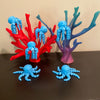 These blue octopi fidgets glow in the dark! 6 blue octopi are resting on a couple of corral reefs. All of the items in the photo are manufactured by Chuganation's 3D Lab.