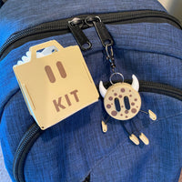 Blue backpack with a gold 'KIT' keychain on a neutral background