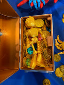 A golden fokobot (robot) fidget designed by flexi factory rests in a treasure chest full of golden coins and jewels. This fokobot fidget was manufactured by Chuganation's 3D Lab.