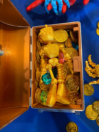 A golden fokobot (robot) fidget designed by flexi factory rests in a treasure chest full of golden coins and jewels. This fokobot fidget was manufactured by Chuganation's 3D Lab.