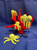 These green octopi fidgets glow in the dark! 5 green octopi are resting on a corral reef. All of the items in the photo are manufactured by Chuganation's 3D Lab.