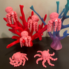 These pink octopi fidgets glow in the dark! 6 pink octopi are resting on a couple of corral reefs. All of the items in the photo are manufactured by Chuganation's 3D Lab.